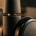 Macro close-up of a black rubber office chair caster wheel connected to a textured plastic base via a polished metal stem, highlighting premium build quality and material durability