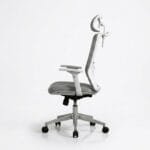 Side profile view of a grey and white ergonomic high-back mesh office chair showing height and angle-adjustable headrest mechanism, full mesh backrest with white frame, multi-directional adjustable armrest, grey fabric seat cushion, chrome gas lift cylinder, and silver aluminum five-star base with black caster wheels, on white background